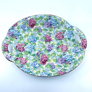 May include: A white oval serving tray with two handles. The tray is decorated with a floral pattern of blue, purple, and pink hydrangeas on a light green background.