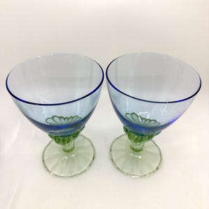 K&ouml;nnte beinhalten: Zwei transparente Weingl&auml;ser mit blauem Rand und hellblauem Kelch. Der Fu&szlig; ist gr&uuml;n mit einem floralen Design. Der Stiel ist gr&uuml;n und der Fu&szlig; hellgr&uuml;n.