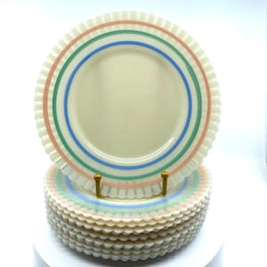 May include: A stack of cream-colored plates with a ruffled edge. Each plate features three horizontal stripes in pink, green, and blue. The plates are stacked on a gold-colored plate stand.