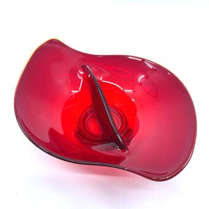 May include: A red glass serving bowl with a divided center section. The bowl has a wavy, organic shape.