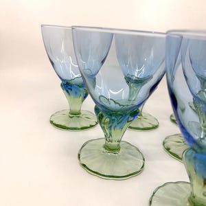 K&ouml;nnte beinhalten: Ein Satz von sechs Vintage-Weingl&auml;sern. Die Kelche sind hellblau, mit gr&uuml;nen und blauen Stielen und F&uuml;&szlig;en. Die F&uuml;&szlig;e sind rund mit einem gewellten Rand. Die Gl&auml;ser sind auf einer wei&szlig;en Oberfl&auml;che angeordnet.