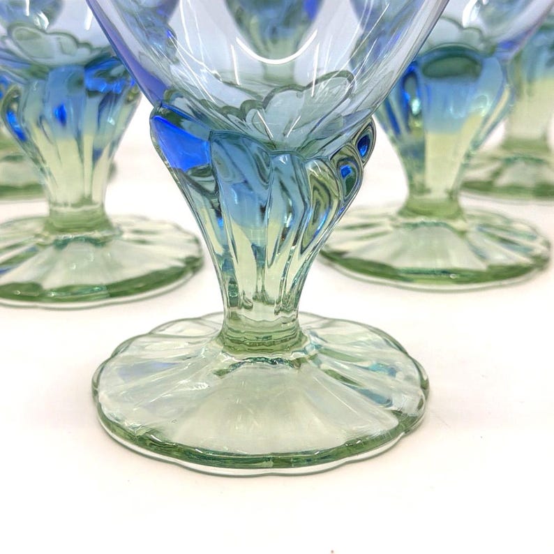 K&ouml;nnte beinhalten: Ein Set aus blauen und gr&uuml;nen Dessertschalen aus Glas im Vintage-Stil. Die Stiele haben ein geriffeltes Design, und die B&ouml;den sind gewellt. Das Glas hat einen subtilen Schimmer, wobei sich die blaue Farbe im oberen Teil der Gl&auml;ser konzentriert.
