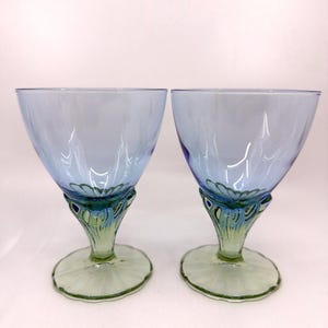 K&ouml;nnte beinhalten: Zwei elegante blaue Weingl&auml;ser mit einzigartigem Design. Die Kelche sind hellblau, mit einem dekorativen Stiel mit gr&uuml;nen und blauen Akzenten. Der Fu&szlig; ist hellgr&uuml;n. Ideal f&uuml;r besondere Anl&auml;sse.