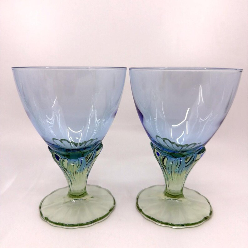 K&ouml;nnte beinhalten: Zwei elegante blaue Weingl&auml;ser mit einzigartigem Design. Die Kelche sind hellblau, mit einem dekorativen Stiel mit gr&uuml;nen und blauen Akzenten. Der Fu&szlig; ist hellgr&uuml;n. Ideal f&uuml;r besondere Anl&auml;sse.