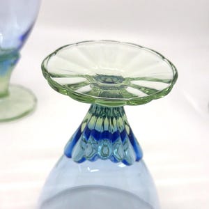 K&ouml;nnte beinhalten: Nahaufnahme eines Glasbechers mit hellblauer Schale und dekorativem Stiel. Der Stiel geht von Blau in Gr&uuml;n &uuml;ber, mit einer gewellten gr&uuml;nen Basis, die eine klare, gewellte Oberseite tr&auml;gt.