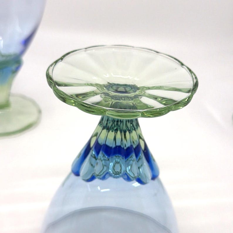 K&ouml;nnte beinhalten: Nahaufnahme eines Glasbechers mit hellblauer Schale und dekorativem Stiel. Der Stiel geht von Blau in Gr&uuml;n &uuml;ber, mit einer gewellten gr&uuml;nen Basis, die eine klare, gewellte Oberseite tr&auml;gt.