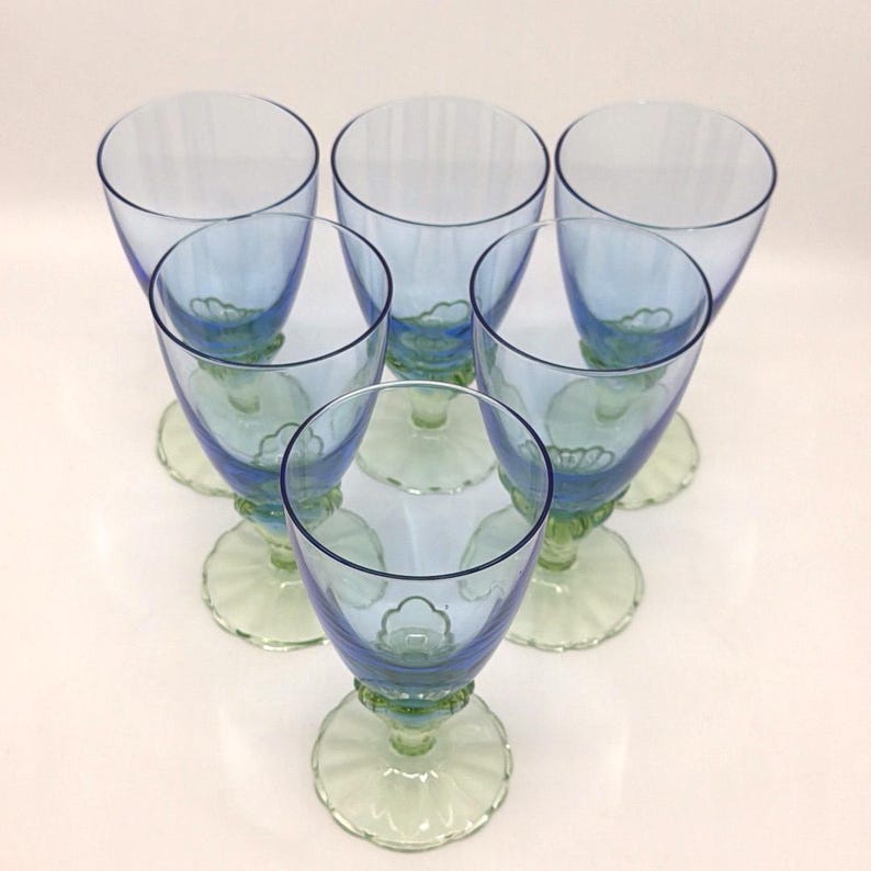 K&ouml;nnte beinhalten: Sechs Vintage-Stielgl&auml;ser in Blau und Gr&uuml;n, kreisf&ouml;rmig angeordnet. Die Gl&auml;ser haben eine hellblaue Schale, einen gr&uuml;nen Stiel und einen gewellten Fu&szlig;. Die Stiele haben ein dekoratives Blumenmuster.