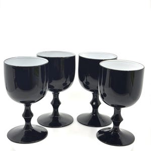 May include: Set of four black wine glasses with a glossy finish and white interiors. Each glass features a rounded bowl, a slender stem, and a circular base. The glasses are arranged on a white background, showcasing their elegant design.