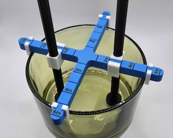 May include: A blue and white candle making tool with two black rods and a clear glass jar. The tool has markings in inches from 1 to 6.