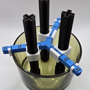 May include: A 3D-printed tool with black vertical posts and blue and white measuring arms. The arms are labeled with measurements in inches. The tool is designed to be used inside a clear glass container.