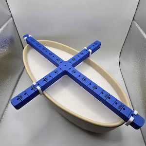 May include: A blue plastic candle centering tool with white clips. The tool has markings in inches from 1 to 10. The tool is placed inside a white oval ceramic bowl.