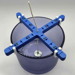 May include: Blue candle centering tool with white clips, marked in 1/2 inch increments, holding a wick centered in a clear glass jar.