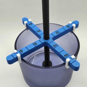 May include: A blue and white 3D printed tool for measuring the depth of a container. The tool has four arms that extend out from a central rod. Each arm has a ruler marked in inches. The tool is sitting in a clear glass container.