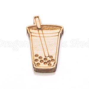 May include: A wooden laser-cut charm in the shape of a bubble tea cup with a straw. The charm is light brown with etched details showing the cup's outline, the straw, and the boba pearls at the bottom. The charm is on a white background.