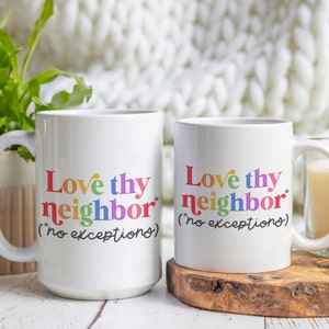 Puede incluir: Dos tazas de cerámica blanca con el texto "Love thy neighbor* (*no exceptions)" en colores arcoíris. La taza de la izquierda tiene el texto en un tamaño de fuente más grande que la taza de la derecha.