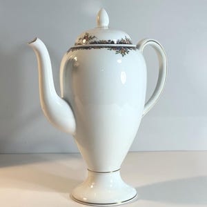 May include: A white porcelain coffee pot with a lid and a curved spout. The pot has a floral design around the rim and gold trim. The pot is approximately 25 cm tall.