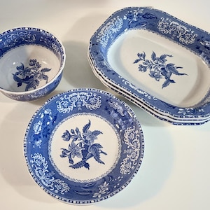 Puede incluir: Un conjunto de vajilla de cerámica azul y blanca con diseños florales. El juego incluye un cuenco redondo, un plato hondo y una pila de fuentes ovaladas. Los bordes de los platos tienen un patrón decorativo.