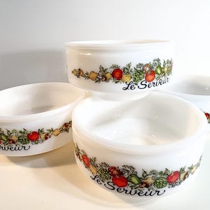 Puede incluir: Un juego de cuatro cuencos de vidrio lechoso blanco con un colorido patrón de verduras en el exterior. Cada cuenco muestra un diseño repetitivo de tomates rojos, alcachofas verdes y cebollas amarillas, junto al texto cursivo negro Le Serveur.