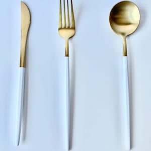 May include: A set of three gold-colored flatware with white handles. The set includes a knife, fork, and spoon.
