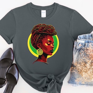 Pode incluir: Uma camiseta cinza escura com uma ilustração colorida de uma mulher com tranças vermelhas e um brinco dourado. A mulher está olhando para o lado e tem os olhos fechados. O fundo é um círculo amarelo e verde.