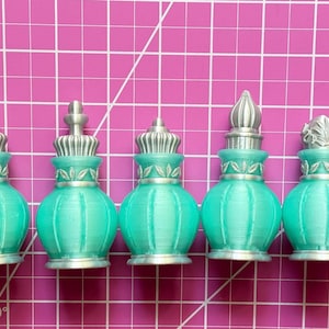 May include: Five small, teal-colored bottles with silver-toned caps and decorative silver collars. Each bottle features a rounded body with vertical ridges and a distinct, ornate silver topper, showcasing varied shapes and intricate detailing.