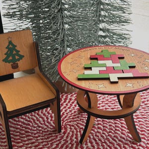 May include: A wooden chair and a round table with a puzzle shaped like a Christmas tree. The chair back features a green tree graphic. The table surface displays the text "Believe in ELF Magic" and is decorated with star outlines and a puzzle.