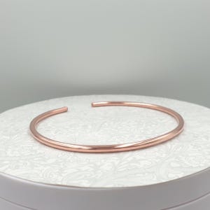 Puede incluir: Un brazalete abierto de oro rosa. El brazalete tiene un diseño simple y minimalista con un acabado liso y pulido. Los extremos abiertos permiten un fácil uso y ajuste. El brazalete tiene aproximadamente 6,35 cm de diámetro.