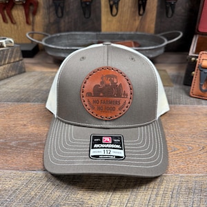 May include: A gray and white trucker hat with a brown leather patch that says "No Farmers No Food" and a tractor image. The hat is adjustable and has a Richardson 112 label.