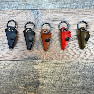 May include: Five leather keychains in different colors: black, brown, red, and green. Each keychain has a small, triangular leather pouch with a metal ring.
