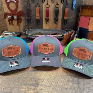 May include: Three gray and black baseball caps with a brown leather patch that says "D-DFARMS EST. 2019". The caps have different colored mesh panels: turquoise, pink, and green.