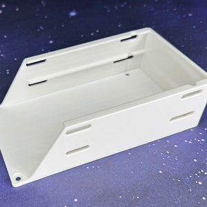 May include: A white plastic box with slots on the sides and a smooth, flat surface. The box is empty and appears to be for storage or organization.