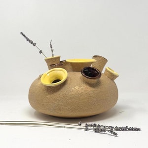 May include: A ceramic vase with multiple openings for flowers, featuring a textured brown surface and yellow and brown accents.