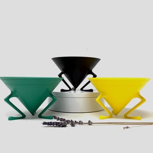 May include: A set of three ceramic mugs with a speckled, matte finish. The mugs are in cream, light grey, and dark grey. Each mug has a simple, minimalist design, ideal for coffee or tea.