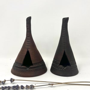 May include: Two small, brown ceramic incense burners shaped like teepees. The burners have intricate designs and a small opening at the top.