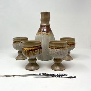 May include: A set of four ceramic drinking cups with a brown and white glaze, and a matching ceramic decanter with a brown and white glaze.