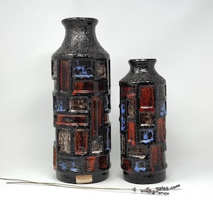 May include: Two ceramic vases with a geometric pattern in shades of brown, red, and blue. The vases are textured and have a rustic look.