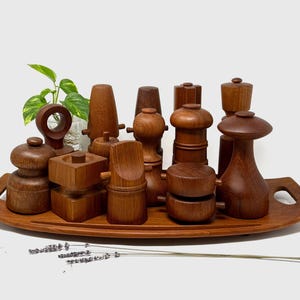 以下が含まれることがあります： 木製のキッチンツール、塩コショウ挽き器、その他の装飾品など、さまざまなものが木製のトレイに並んでいます。アイテムは温かみのある茶色の木材で作られており、自然な仕上がりです。小さな植物とラベンダーの小枝も含まれています。