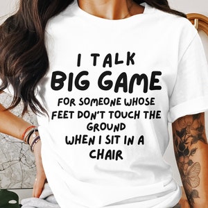 Puede incluir: Camiseta blanca con texto negro que dice "Hablo de grandes juegos para alguien cuyos pies no tocan el suelo cuando me siento en una silla."