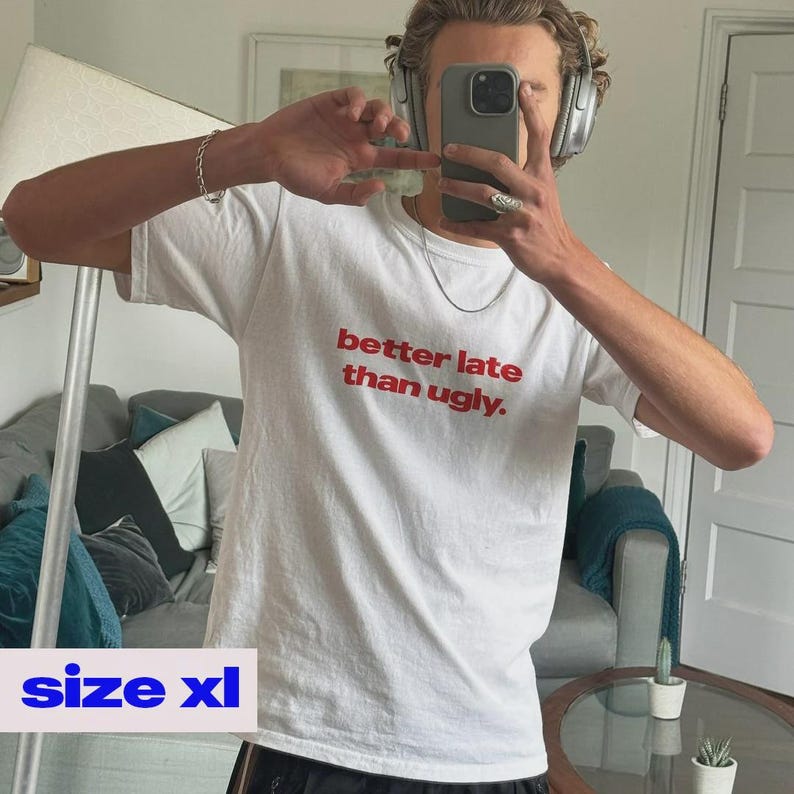 May include: White XL t-shirt with the red text "better late than ugly." The shirt is a classic crew neck style. The image shows a person wearing the shirt.