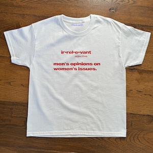 May include: White t-shirt with red text that reads "irrelevant adjective men's opinions on women's issues."
