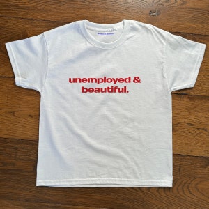 May include: White t-shirt with the text "unemployed & beautiful." printed in red.