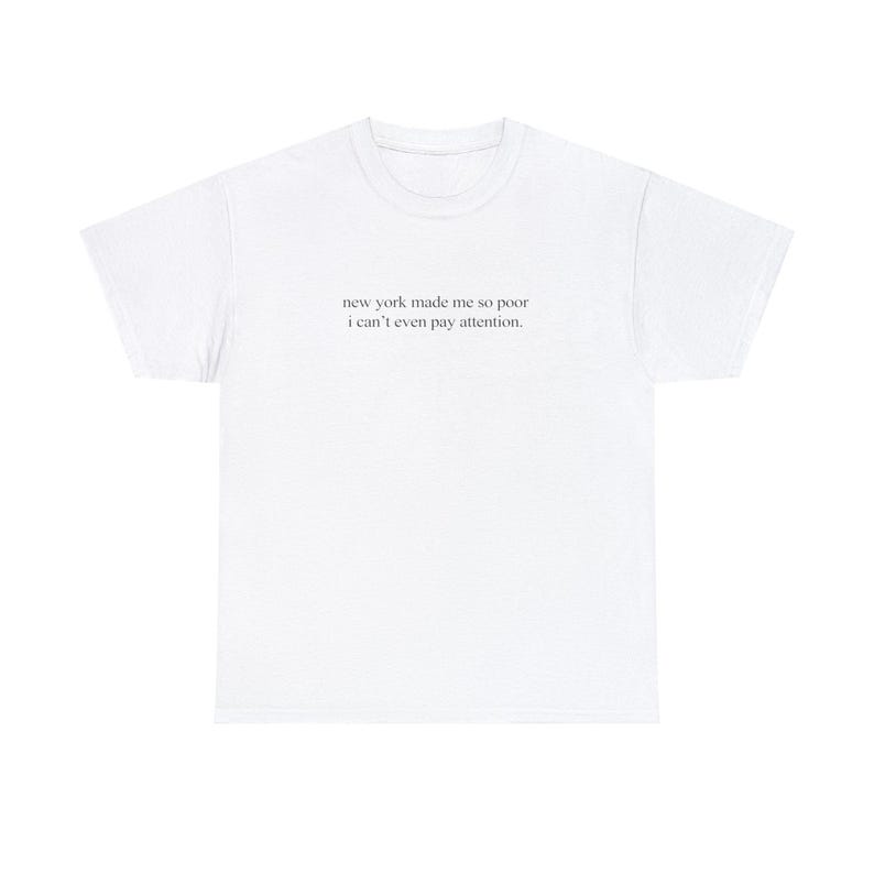 Op de afbeelding: Wit T-shirt met de tekst "new york made me so poor i can't even pay attention."