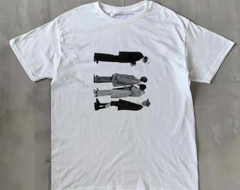 May include: White t-shirt with a black and white graphic print of four people standing in a line. The text "where is charlie" is printed on the shirt.