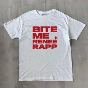 Könnte beinhalten: Weißes T-Shirt mit dem Text "BITE ME RENEE RAPP" in roten, fetten Buchstaben. Ein roter Stern befindet sich neben dem Wort "ME". Das Shirt hat einen Rundhalsausschnitt und ist aus weichem Material.