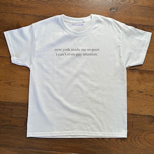 May include: White t-shirt with the text "when in doubt" printed on the neck label and the text "new york made me so poor i can't even pay attention." printed on the front.