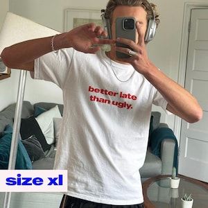 May include: White XL t-shirt with the text "better late than ugly" in red. The shirt is short-sleeved and has a crew neck. The image shows the shirt being worn.