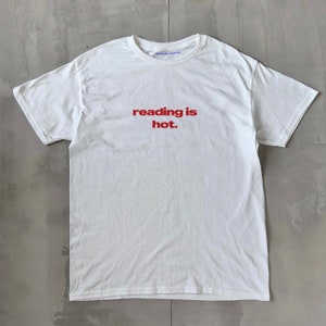 May include: White t-shirt with red text that reads "reading is hot."
