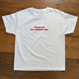 Op de afbeelding: Wit T-shirt met de tekst "teach me the offside rule." in rood gedrukt.