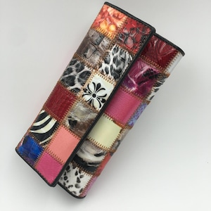 Peut inclure: Une pochette patchwork avec une variété de textures et de motifs. La pochette présente des carrés de cuir rouge, rose, marron et noir avec des imprimés animaliers et des motifs floraux. Les bords sont bordés de noir.