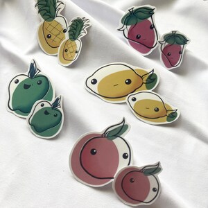 May include: A set of nine colorful fruit stickers with cute faces. The stickers feature pineapples, strawberries, apples, peaches, and fish.